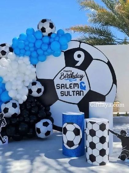 An outdoor football-themed party for a 9th birthday. The large football backdrop is flanked by blue, black, and white balloons and soccer-themed props.