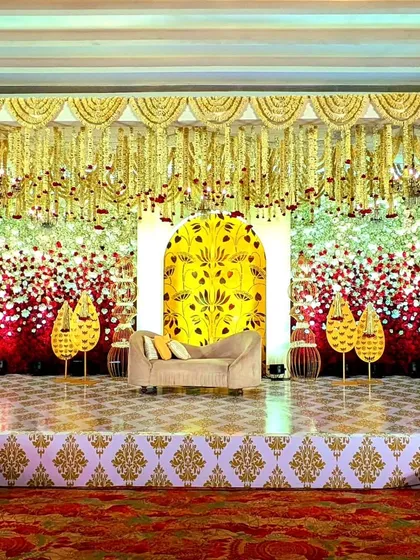 This opulent stage features a wall of red and white roses, a canopy of hanging golden tassels, and a central arch with a traditional yellow floral motif.