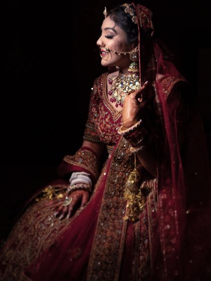 A dramatic and artistic portrait of a bride in her traditional red lehenga. The lighting highlights the rich details of her attire and her graceful pose.