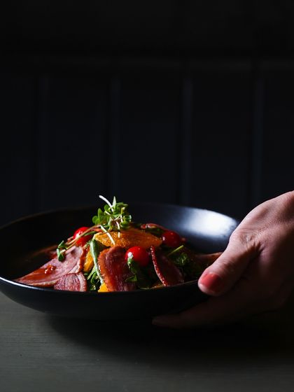 Experience culinary excellence at its finest. A server presents a beautifully arranged smoked duck salad, showcasing the quality and care we put into every plate.
