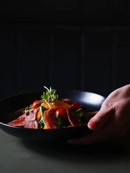 Experience culinary excellence at its finest. A server presents a beautifully arranged smoked duck salad, showcasing the quality and care we put into every plate.