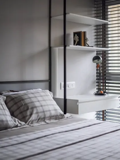 This bedroom features a custom-designed suspended shelving unit that doubles as a bedside table. The clean lines and combination of black metal and white shelves create a modern, functional, and space-saving solution.