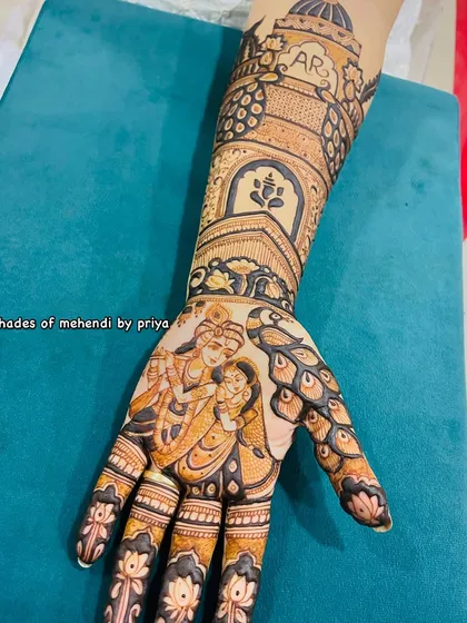 A close-up of a bridal palm featuring a Radha Krishna portrait. The surrounding design uses peacock feather motifs and detailed finger work, creating a divine and beautiful look.
