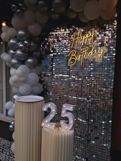 A closer look at the 25th birthday shimmer wall, with the marquee numbers and neon sign glowing.