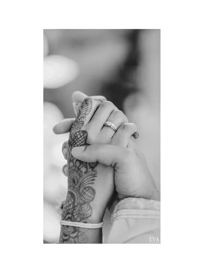A black and white close-up of the couple's hands, showcasing the engagement ring and intricate henna design.