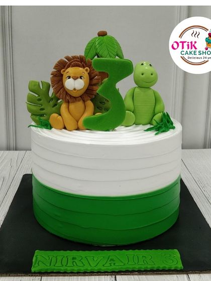 A simple yet charming jungle cake for a third birthday. This design features a clean, two-tone green and white buttercream base, topped with cute fondant figures of a lion and dinosaur.