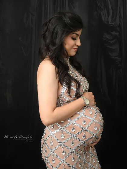 A classic profile shot showcasing the beautiful baby bump. The intricate, sparkling details of the gown are highlighted against a simple black backdrop.