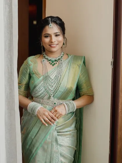 A bride in a beautiful pastel green Kanchipuram saree. Her custom blouse features a unique scalloped neckline and detailed embroidery, perfectly matching her diamond and emerald jewelry.