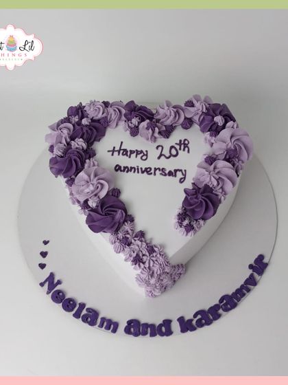 A lovely heart-shaped cake celebrating a 20th anniversary. The heart is outlined with a beautiful ombre of purple-piped flowers.