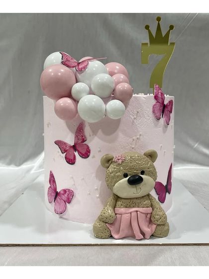 A tall cake for a 7th birthday, featuring a hand-molded fondant teddy bear, pink butterflies, and chocolate spheres.