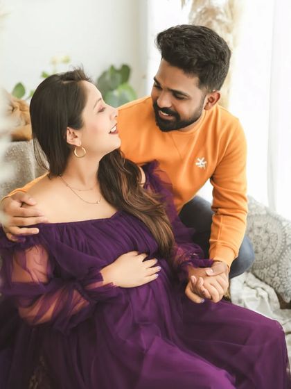 A moment of shared joy and affection. The warm tones of their outfits and the soft studio light create a cozy and intimate atmosphere for this maternity photo.