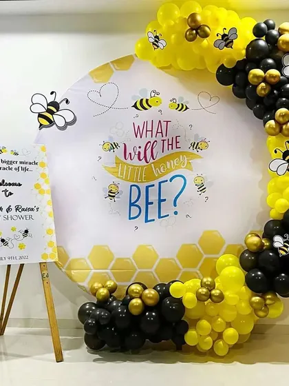 A 'What will the little honey bee?' gender reveal party with a bee-themed backdrop and a black and yellow balloon arch.