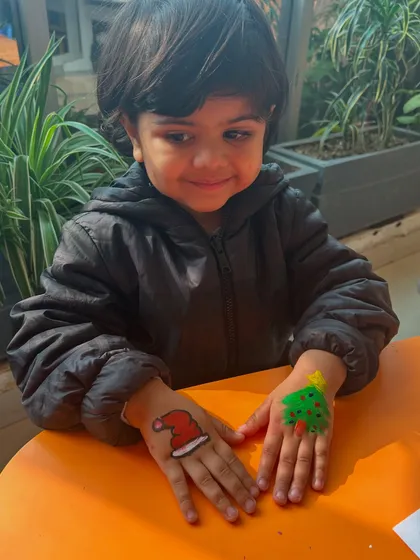 Look at that festive face paint! A young boy proudly shows off the Christmas tree and Santa hat painted on his hands, adding to the holiday fun.