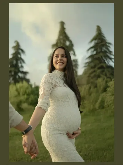 Her smile radiates pure joy as she is led by her partner through a sunlit park. This image captures a candid, happy moment, focusing on the excitement and love of the mother-to-be.