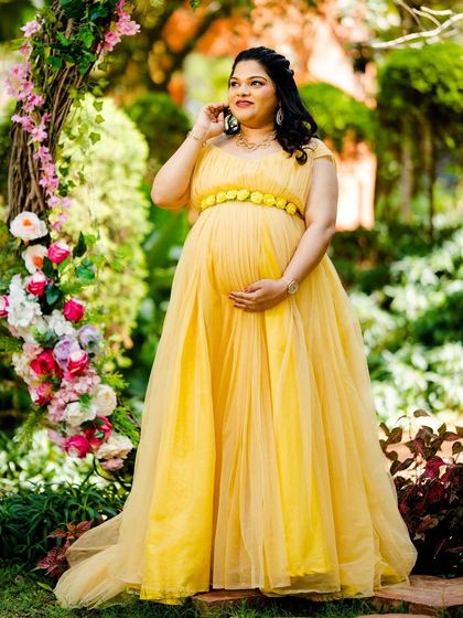 A full-length solo maternity portrait by the floral arch.