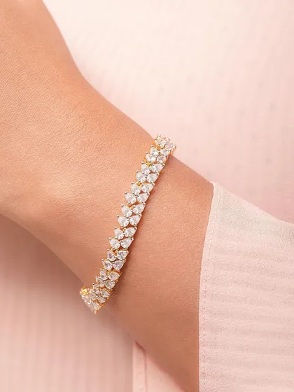 A close-up shot of a sparkling diamond-style bracelet on a model's wrist against a soft pink fabric. This highlights the piece's elegance and shine.