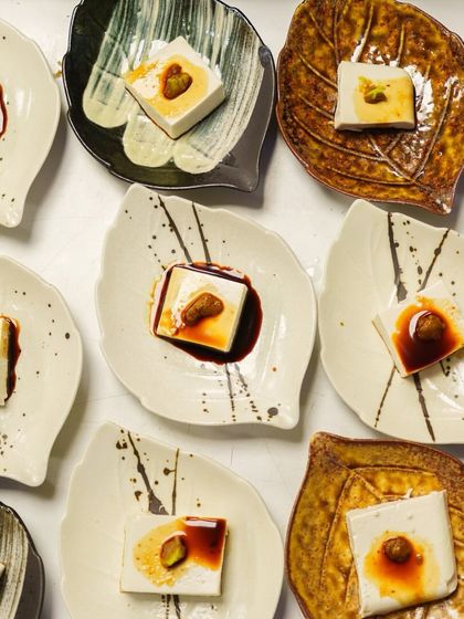 An array of Hiyayakko, or chilled tofu, appetizers. Each piece is served on a unique, leaf-shaped dish and topped with a savory garnish and soy sauce.