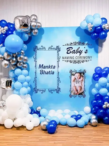I create beautiful and personalized decorations for traditional events like this baby's naming ceremony. This setup includes a custom-printed backdrop with the baby's name and photo, framed by a stylish blue, white, and silver balloon arrangement.