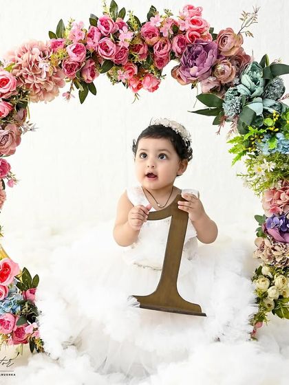 A beautiful floral arch frames this little one perfectly. Sitting among the clouds, she holds the number '1', marking her very special birthday.