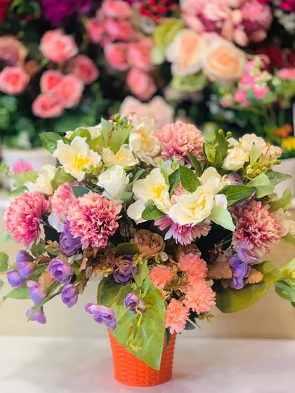 A beautiful artificial flower arrangement in a small orange pot. This mix of faux carnations and tulips in pastel shades is perfect for a desk or side table.