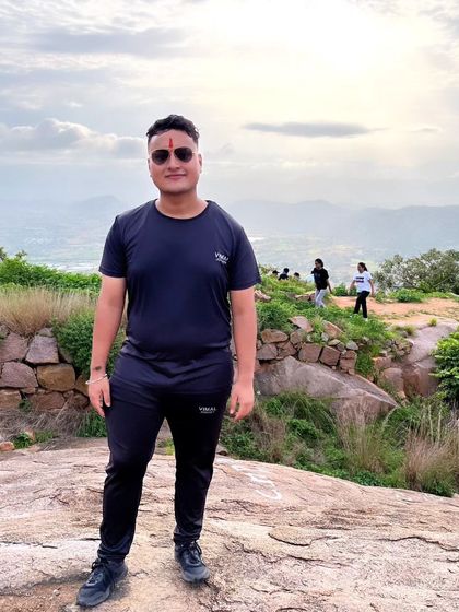 A trekker posing proudly at the Makalidurga viewpoint, with the vast, hilly landscape stretching out behind him.