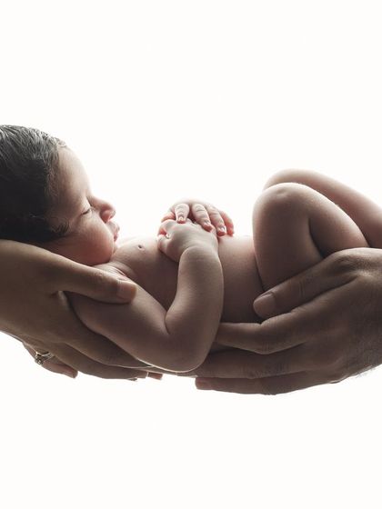 In safe hands. A simple, high-key portrait showing a newborn held securely by both parents' hands, symbolizing their new world of love and protection.