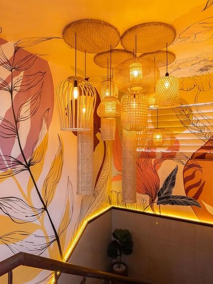 We transformed this restaurant staircase into an immersive art installation. The walls are covered in a warm, yellow-toned mural, and a cluster of bamboo and wicker lights adds a sculptural element.