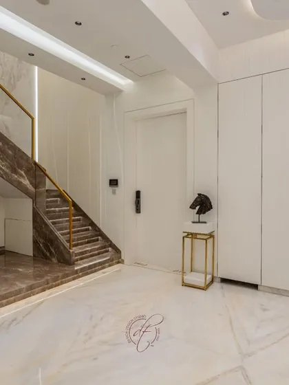 This wide shot shows the living area's connection to the grand staircase and the rest of the open-plan ground floor. The consistent marble flooring unifies the entire space.