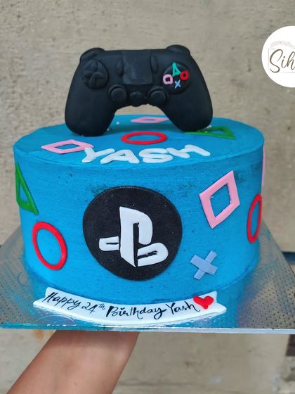 A cake for a PlayStation fanatic. This bright blue cake is decorated with the iconic controller symbols and a hand-sculpted fondant controller on top.