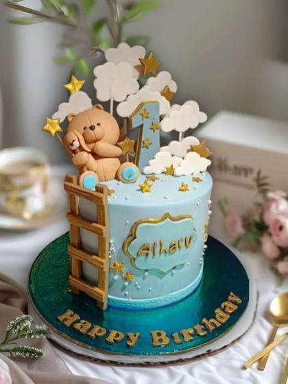 A sweet first birthday cake featuring a teddy bear climbing a ladder to the clouds and stars, creating a dreamy, celestial theme.