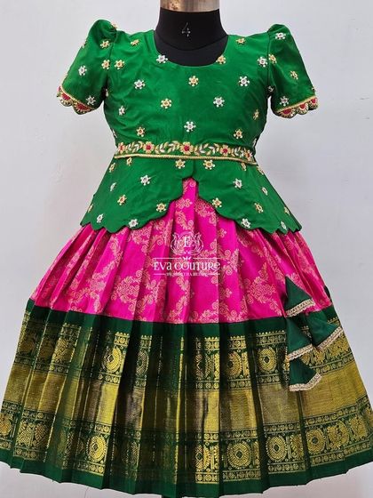 A classic green and pink Pattu Pavadai. The blouse has delicate white floral embroidery, and the skirt is a pink brocade with a green and gold border.
