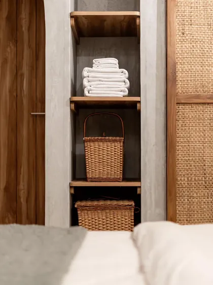 A detail shot of bedroom storage, featuring open wooden shelves and woven baskets. The combination of wood, wicker, and concrete-finish walls creates a rustic yet modern aesthetic.