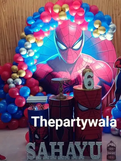 A huge Spiderman backdrop makes a big impact! This setup for a 6th birthday party uses a massive character graphic, themed pedestals, and a colorful balloon arch with red, blue, and gold balloons.