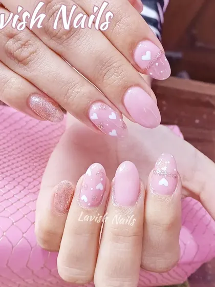 An overlay on natural nails, featuring a soft pink base with tiny white hearts and a glitter accent.