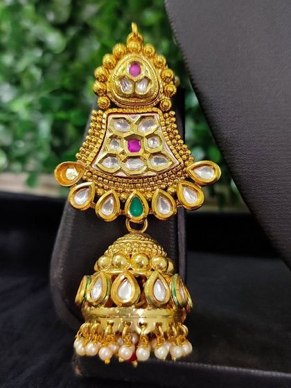 A detailed view of an earring from the for-sale set in image 40. The piece showcases kundan work with pink and green stones and a classic jhumka drop.