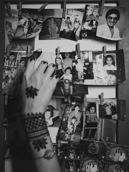 A creative shot from an at-home mehendi, with the bride's henna-adorned hand against a backdrop of old family photos. This reflects our philosophy of weaving personal history into wedding celebrations.