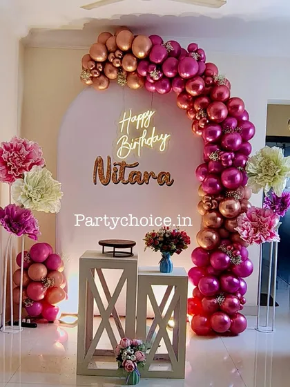 A glamorous birthday decoration for an indoor home party. The metallic balloon arch and neon sign create a festive and chic atmosphere.