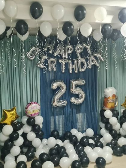 A black and white themed room decoration for a 25th birthday. This setup includes balloon pillars, ceiling balloons, and a curtain backdrop for a chic and modern party at home.
