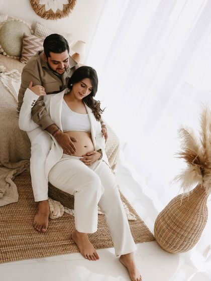A modern and intimate pose. The white pantsuit paired with the earthy, boho backdrop creates a unique blend of chic style and warm emotion.