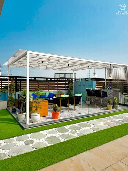 A bright and airy white pergola with a polycarbonate roof, offering protection from rain while letting in sunlight. The space includes a lounge area and a bar, making it a versatile outdoor room.