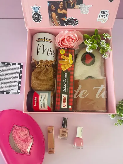 A "Bride to be" hamper in a large pink box. It's filled with goodies like a "Miss to Mrs" mug, shortbread, makeup, and a personalized photo collage.