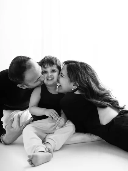 The beauty of black and white photography lies in its ability to focus on pure emotion. This image is filled with love and laughter, as parents shower their son with kisses, creating a powerful and timeless family portrait.