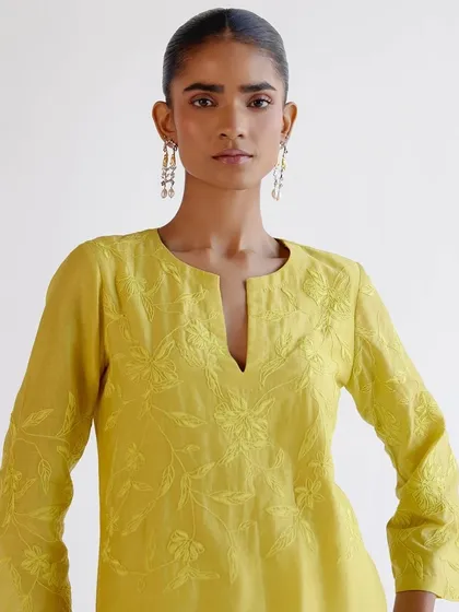 A close-up of a lemon-yellow kurta with tonal floral embroidery. The subtle texture and delicate craftsmanship make this a truly special piece.