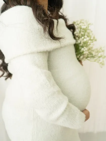 A close-up detail shot focusing on the baby bump and the soft texture of a cozy sweater dress. It's a simple, intimate, and beautiful portrait.