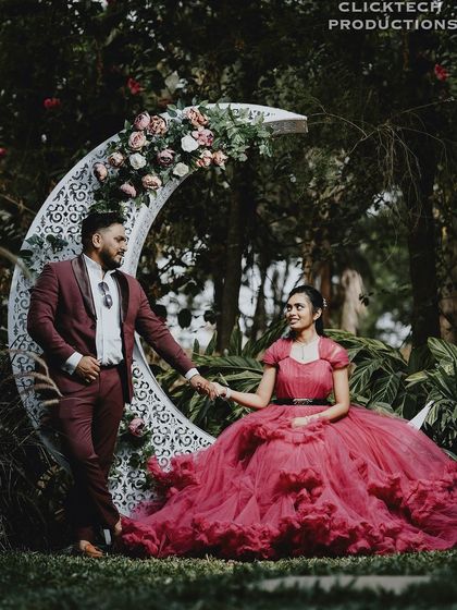 A romantic, fairy-tale shot with the bride in a stunning pink gown, seated on a crescent moon prop, holding hands with her groom.