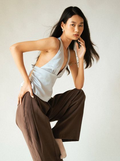 A dynamic, full-body pose in a studio setting. This shot captures a sense of movement and confidence, showcasing the entire outfit from the halter top to the wide-leg trousers.