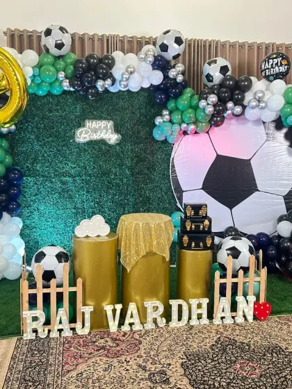 A soccer fan's dream birthday party. This setup includes a faux grass backdrop, a large inflatable soccer ball, cutouts of Cristiano Ronaldo, and a green, black, and white balloon arrangement.