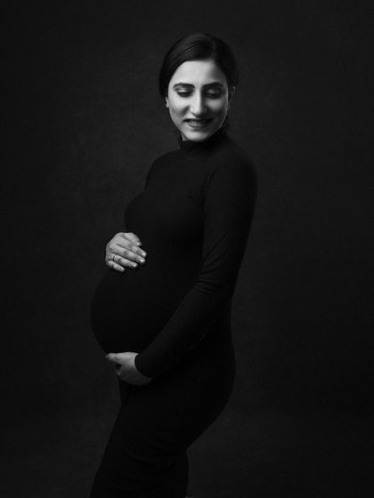 A quiet and gentle moment, her gaze directed lovingly towards her bump. The dark, simple background keeps the focus entirely on her.