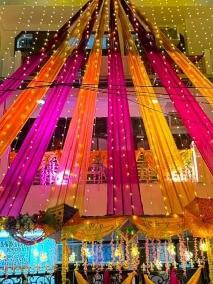 We transform your entire house into a celebration zone. This shows our full-house draping service, where we use colourful fabrics and string lights to decorate the building's exterior, making it look festive day and night.