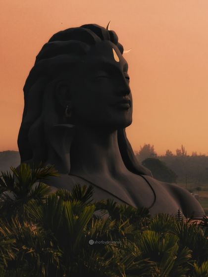 The Adiyogi statue bathed in the warm glow of sunset, seen through the palm trees of Coimbatore.